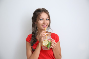 Young woman with mason jar of fresh lemonade on light background
