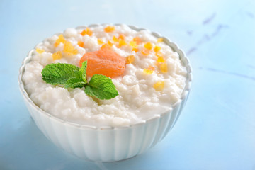 Bowl with delicious rice pudding and dry apricots on color background
