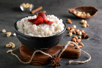 Bowl with delicious rice pudding and strawberry on dark table