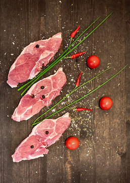 Lamb steaks, tomatoes, onion, chili pepper , salt and junipers seeds on the brown wooden retro plate 