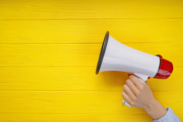 Woman holding megaphone on color wooden background