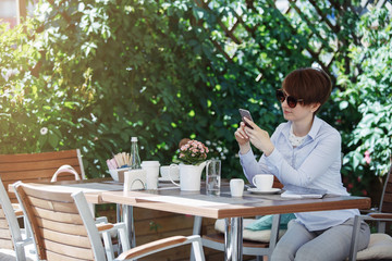 Young cute woman in glasses drinks coffee in a summer cafe.