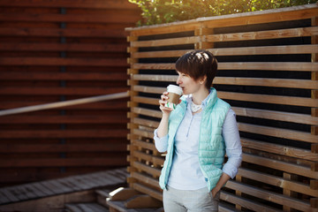 A young pretty woman in a blue jacket is drinking coffee.