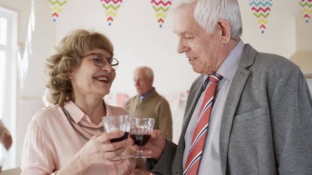 Smiling senior woman chatting with male friend and toasting with wine at cocktail party with friends at home