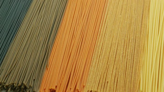 Multicolored organic uncooked spaghetti composed in row on table surface