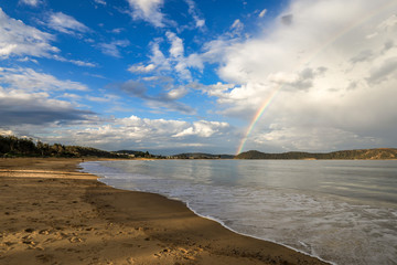 Rainbow over ocean and beach against cloudy blue sky