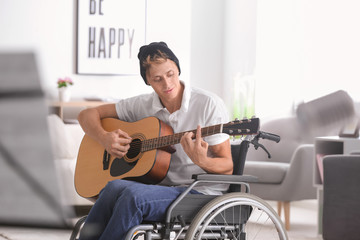Young musician in wheelchair playing guitar at home