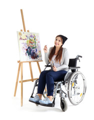 Young female artist in wheelchair painting picture on white background