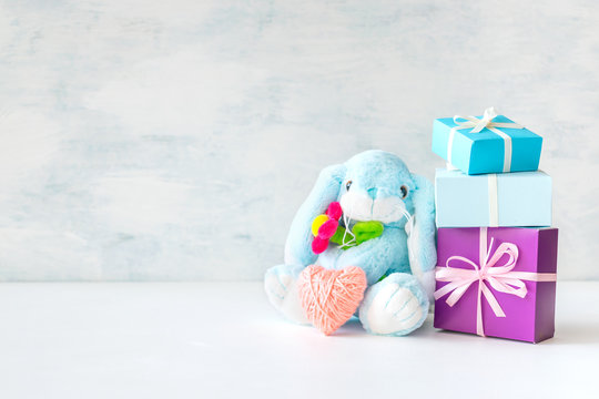 Cute toy soft blue bunny with a flower and pink thread heart with soap bubbles on light background. Birthday card, newborn, mother's day, gift present background.