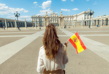 Fototapeta premium nowoczesna podróżniczka z flagą Hiszpanii przeciwko Pałacowi Królewskiemu