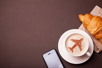Mug of coffee with an airplane on the foam. Morning coffee with croissant in flight. Smrtrfonom and...