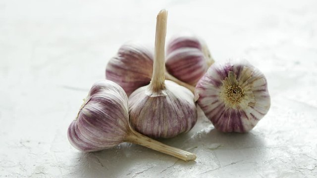 Closeup shot of composed pile of unpeeled garlic bulbs with stems lying on rough white surface in daylight