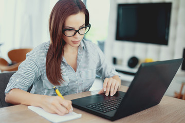 Young clever woman writing notes at laptop