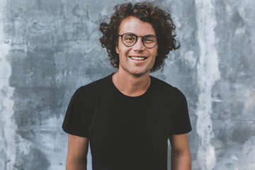 Outdoor portrait of handsome freckled smiling male with curly hair, wears sepctacles posing for...