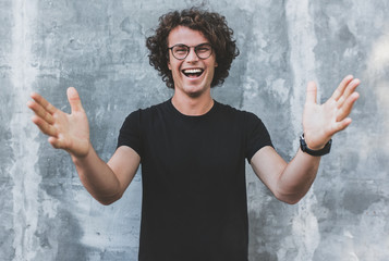 Outdoor horizontal shot of handsome happy smiling male with curly hair, wears sepctacles posing for...
