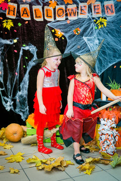 Children, little girls in the form of witches on a broomstick, posing against the backdrop of scenery of cobwebs, pumpkins and autumn leaves for the Halloween feast.