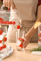 Woman preparing cocktail with cherry tomatoes and ice in kitchen