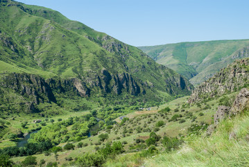 Fototapeta premium Splendid sunny landscape in Georgia. Rocky green mountains and deep blue sky. Grass covering the hills. Mountain river and road