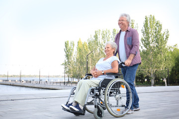 Senior woman in wheelchair and her husband outdoors