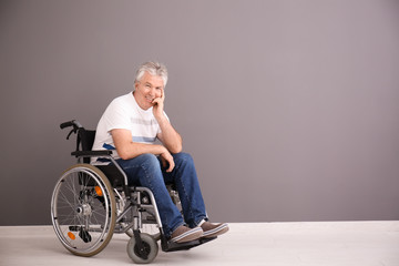 Senior man in wheelchair near grey wall