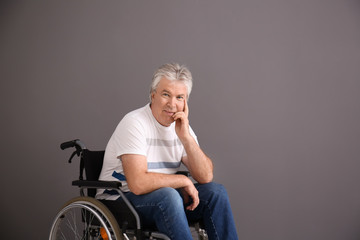 Senior man in wheelchair on grey background