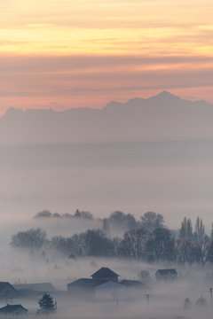 Misty trees and building with mountains and sunrise in the background