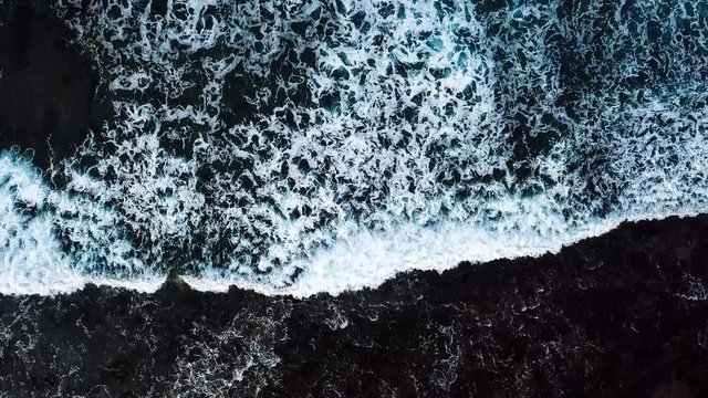 beautiful slow motion wave on the rocky beach in tenerife while a long oceanic foam is coming. aerial footage slow motion landscape and water waves with nobody. vacation outdoor