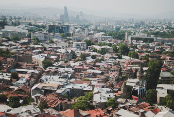 Panoramic view of Old Tbilisi, the capital of Georgia. Cable car over the city. Hot sunny afternoon. Red rooftops of old houses.