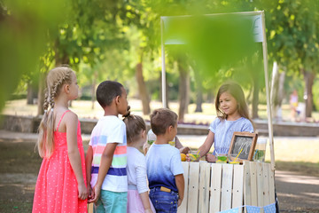 Adorable children waiting in queue for natural lemonade near stand in park