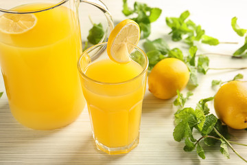 Glass and jug of fresh lemon juice on light wooden table