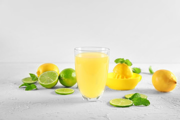 Glass of fresh lemon juice and slices of lime on white textured background