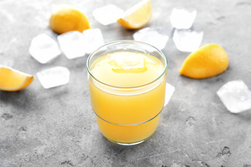 Glass of fresh lemon juice with ice cubes on grey table