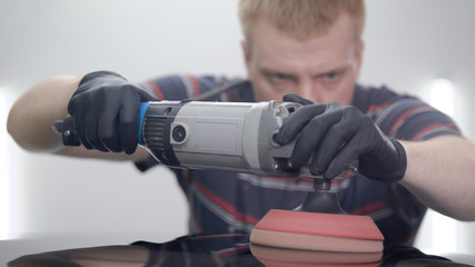 worker is sanding surface of roof of black car in auto-service after repairing work, using electric tool