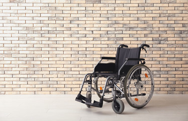 Empty modern wheelchair near brick wall indoors