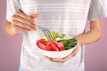 Woman eating tasty salad with watermelon, feta and vegetables on color background, closeup