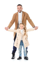 Fototapeta premium father and daughter holding hands and posing in beige coats, isolated on white