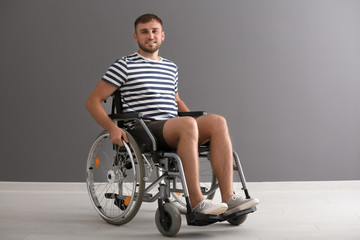 Fototapeta na wymiar Young man in wheelchair against grey wall