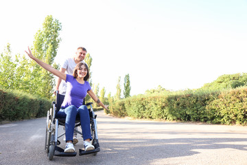 Happy young woman in wheelchair and her husband outdoors