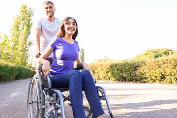 Happy young woman in wheelchair and her husband outdoors