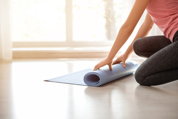 Young woman rolling yoga mat on floor