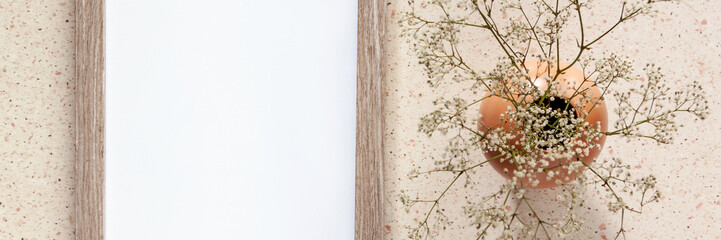 Panoramic photo of terrazzo desk with a wooden mockup frame and a vase with dried white flowers