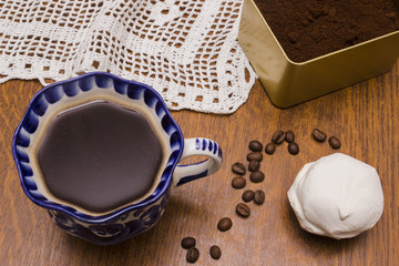 Coffee beans, ground coffee, white marshmallow and cup of brewed coffee on wooden table