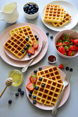 Belgian waffles with strawberries and blueberries on pink plate on gray wooden background. Top view. Copy space