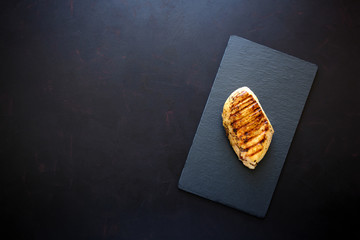 Grilled chicken fillets on slate plate on dark wooden background. Top view. Flat lay. Copy space