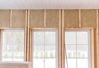 Thermally insulating eco-wood frame house with wood fiber plates and heat-isolating natural hemp material. Finishing the walls and a large window with a white wooden board, using laser line level.