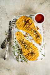 Simple autumn domestic recipes, roasted hasselback butternut squash pumpkin with thyme, honey and maple syrup, on light background copy space top view