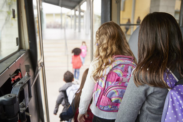 Two girls waiting behind their friends to get off school bus - obrazy, fototapety, plakaty