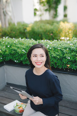 A young cute girl sitting in the park working scrolling a tablet