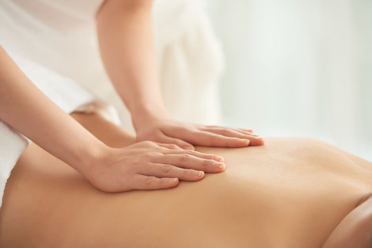 Crop woman massaging back of female client while working in spa salon