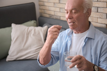 Senior man taking medicine at home